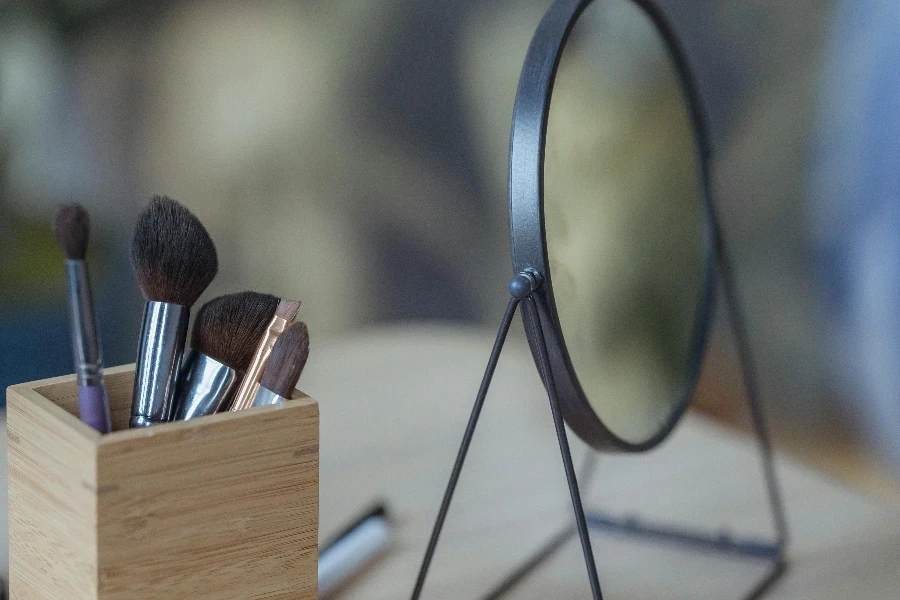 Pinceaux cosmétiques et miroir rond posés sur une table en bois