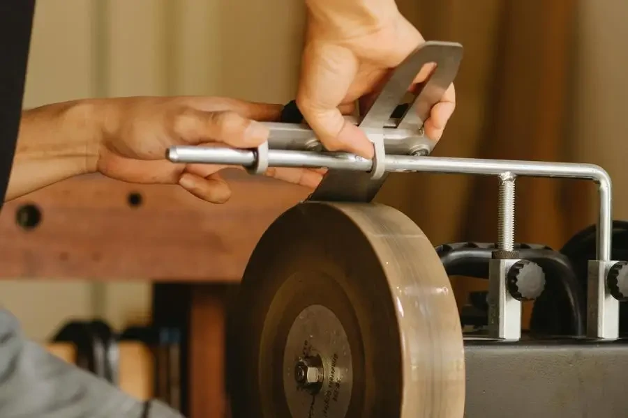 Crop craftsman sharpening tool on grinder in workshop by Ono Kosuki