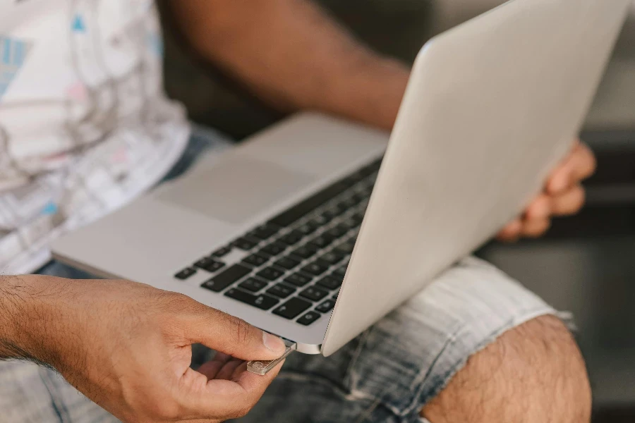 Crop faceless man using laptop and inserting flashcard