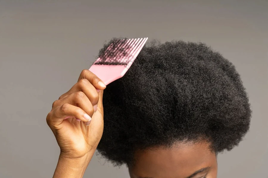 Immagine ritagliata di una mano femminile etnica che tiene una spazzola per capelli sulla testa