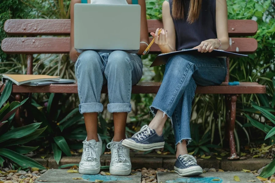 Różnorodni uczniowie korzystają z laptopa do pracy zespołowej na ławce