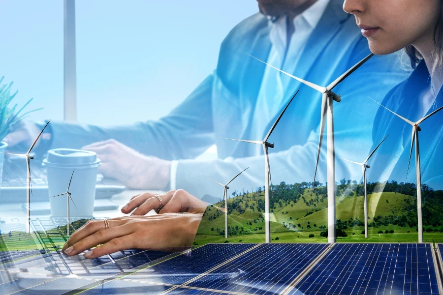 Double exposure graphic of business people working over wind turbine farm and green renewable energy worker interface