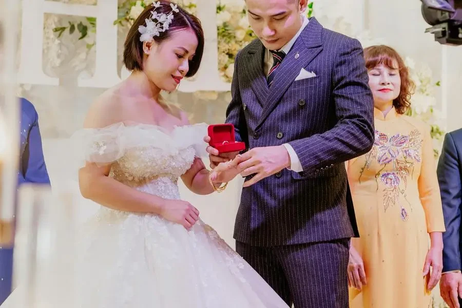 Pria etnik dalam setelan elegan memasangkan cincin di jari wanita tercinta dalam gaun pengantin selama upacara pernikahan oleh HONG SON