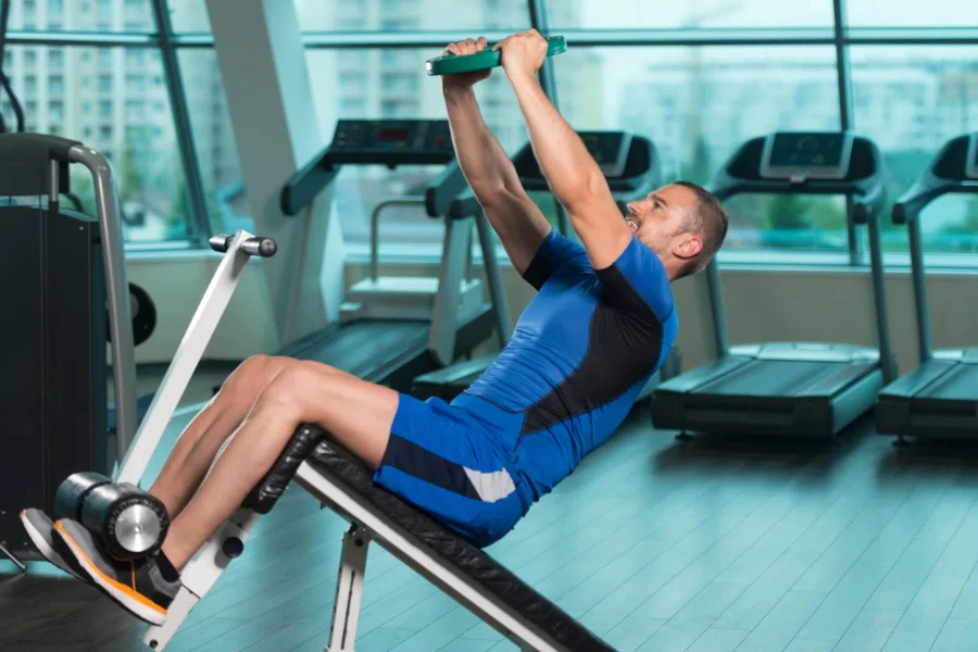 Fitness Man trabajando abdominales con pesas en un banco ajustable en el gimnasio