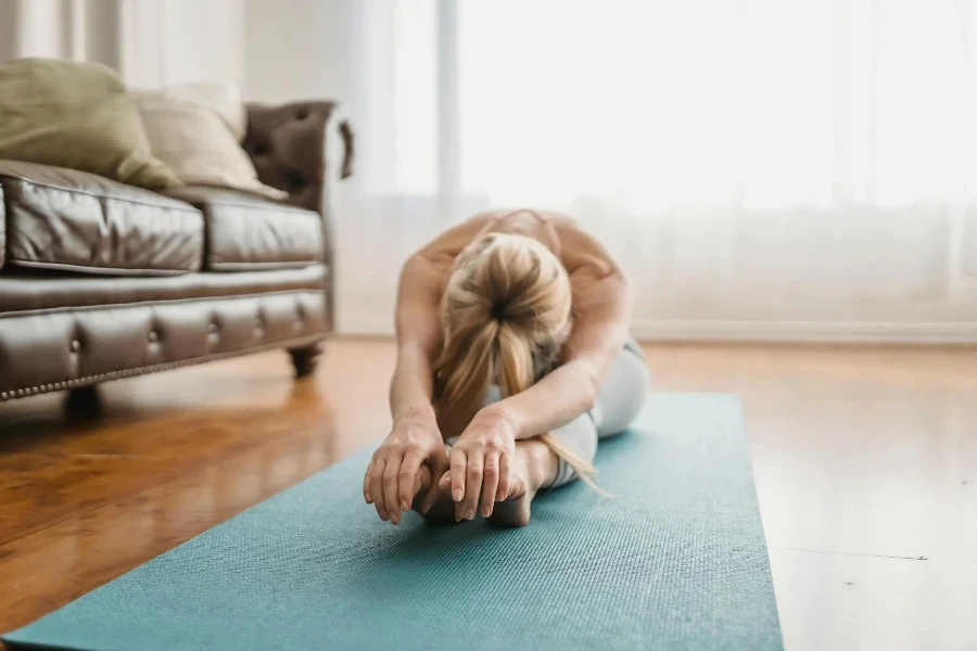 Senhora flexível praticando pose de ioga Pascimottanasana em casa