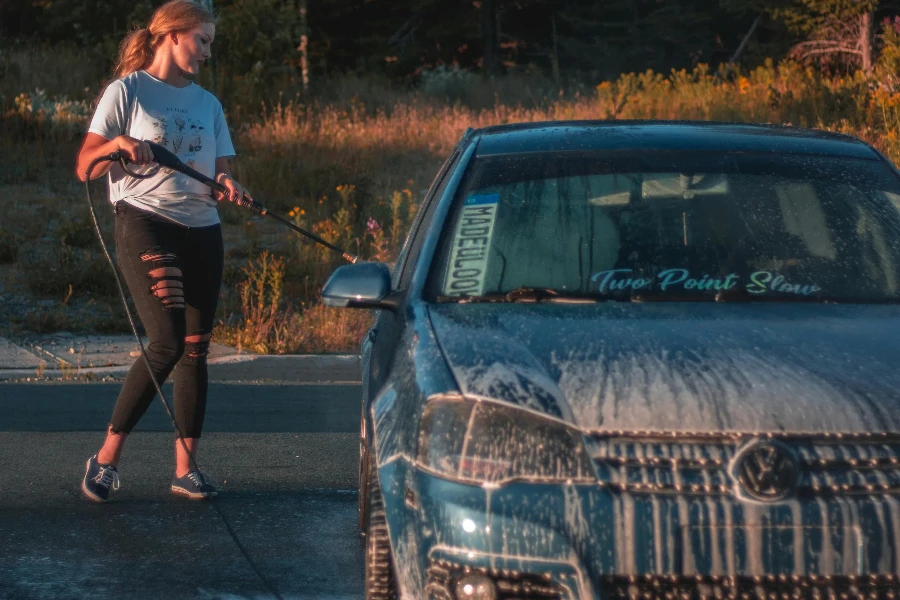 Focused young slender female worker washing automobile parked on pavement