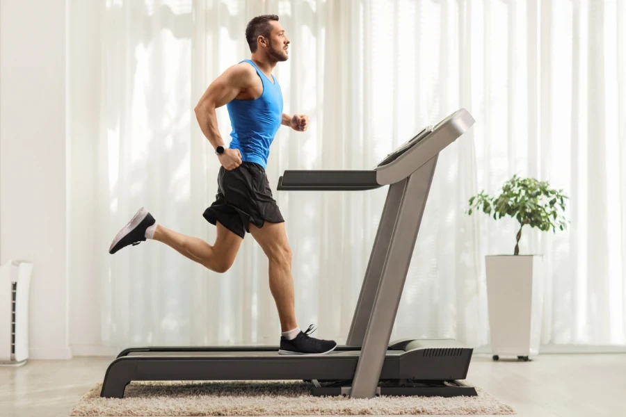 Full length profile shot of a young man running on a treadmill at home