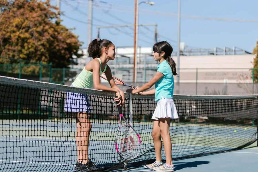 Ragazze che indossano abbigliamento sportivo in piedi accanto alla rete da tennis