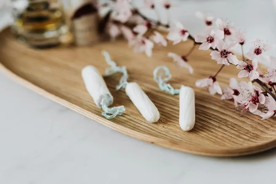 High angle of three menstrual tampons on bamboo plate with flower twig placed against various cosmetic products by Karolina Kaboompics