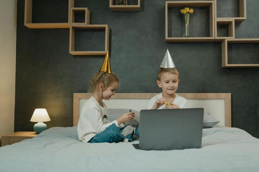 Irmãozinho e irmãzinha usando chapéus de aniversário e sentados na cama