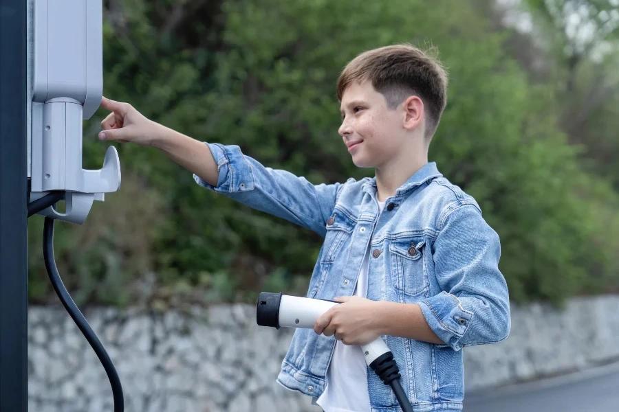 Küçük çocuk, EV şarj istasyonundan çevre dostu elektrikli arabayı şarj ediyor