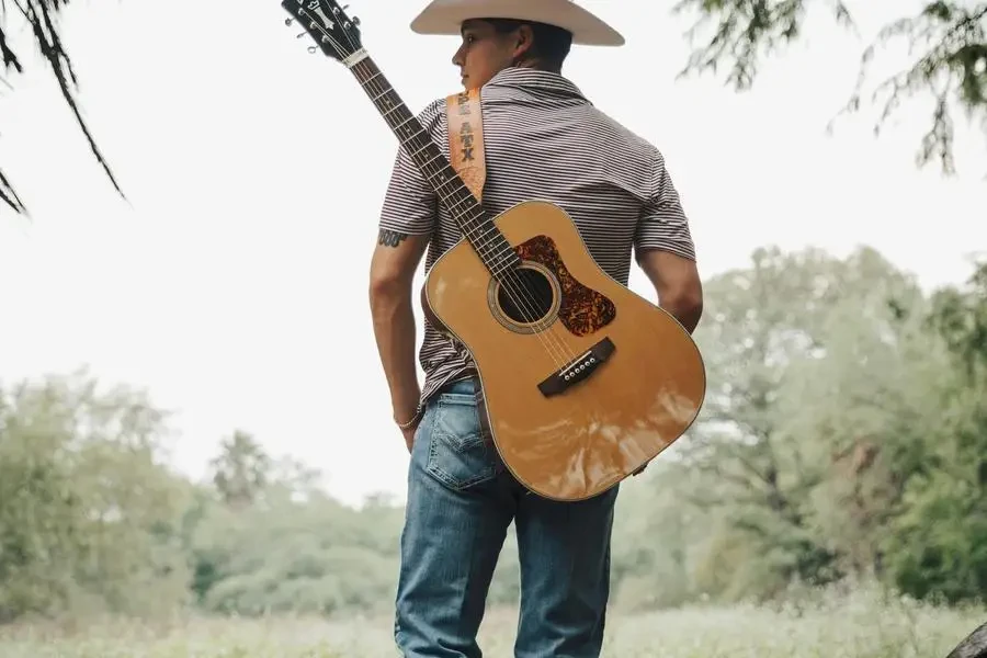 Mann mit Hut und Gitarre auf einer Wiese von Eli Villarreal