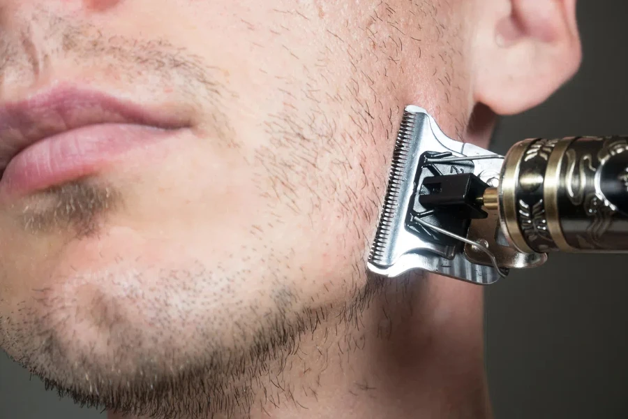 L'uomo taglia la barba con un rasoio elettrico in metallo o un rasoio a secco