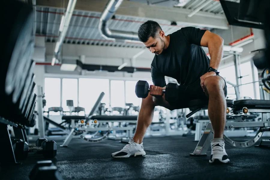 Homme assis sur une machine de gym et faisant des biceps.