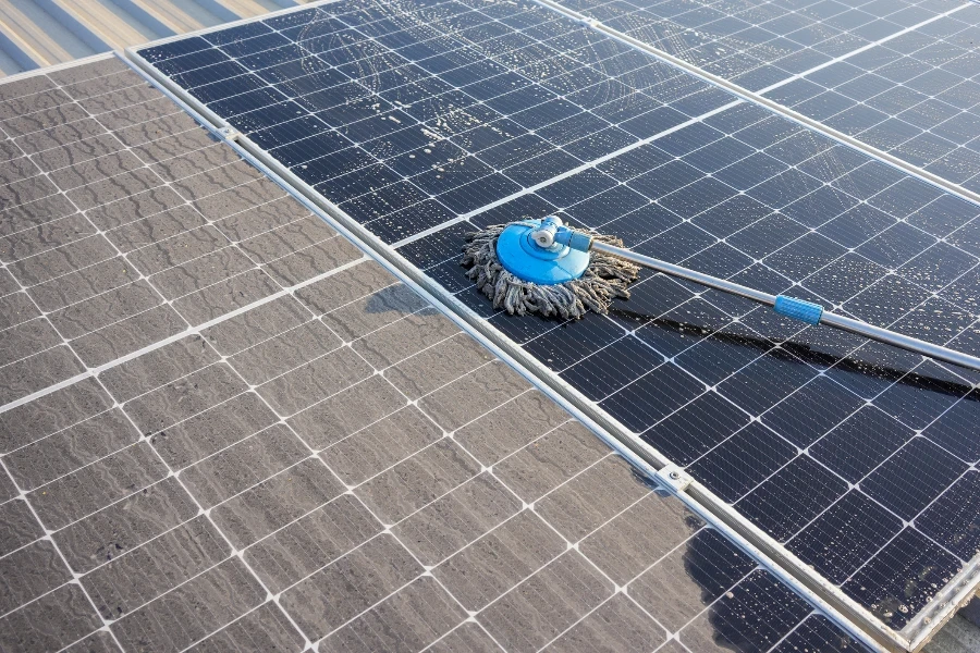 Man using a mop and water to clean the solar panels that are dirty with dust and birds' droppings to improve the efficiency of solar energy storage