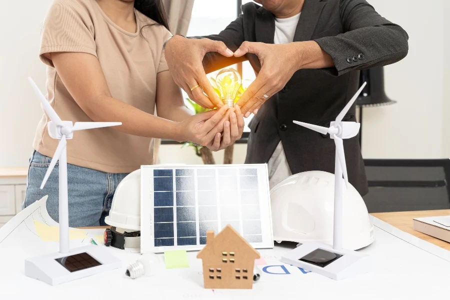 Hombres y mujeres crean formas de corazón con manos alegres y respetuosas del medio ambiente que muestran turbinas eólicas y baterías solares e introducen energía renovable.