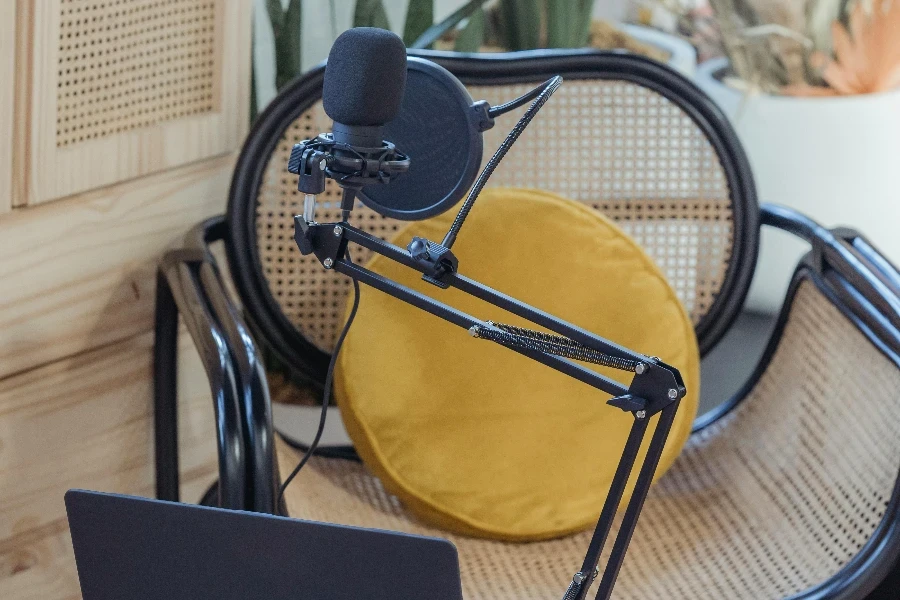 Computadora portátil moderna y micrófono sobre trípode colocados cerca de una silla de mimbre en un estudio moderno antes de grabar un podcast