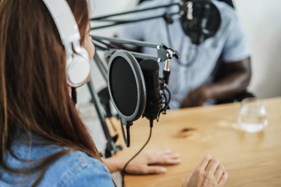 Apresentadores multirraciais fazendo entrevistas enquanto transmitem podcast juntos no home studio - Concentre-se no microfone