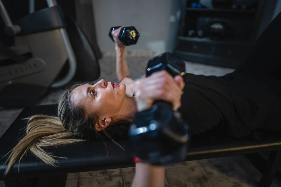 Seorang wanita dewasa tangan langsing wanita Kaukasia memegang dumbbell saat berlatih di rumah