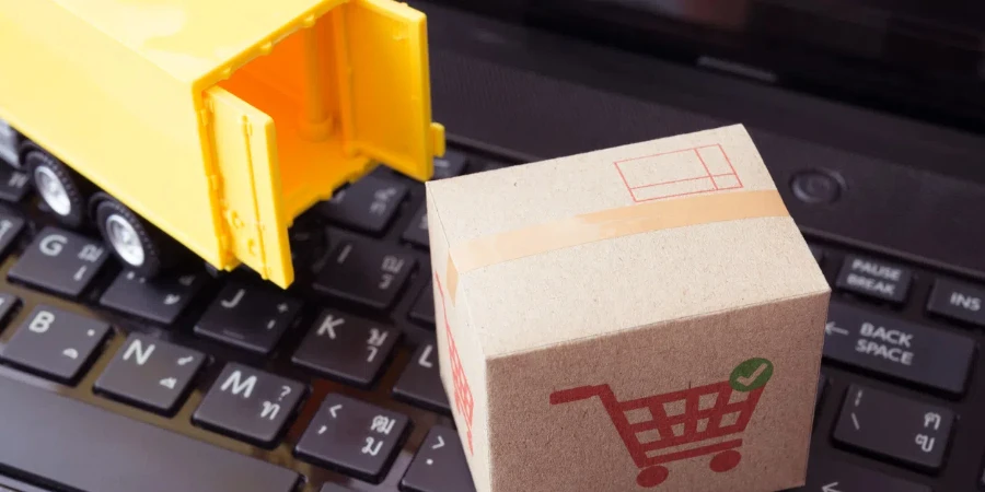 Картонная коробка для посылок с печатью тележки для покупок и грузовиком доставки на фоне ноутбука