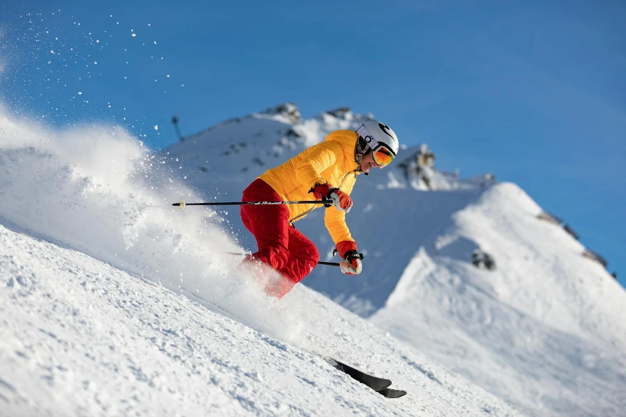 Человек в желтой куртке и красных штанах катается на лыжах