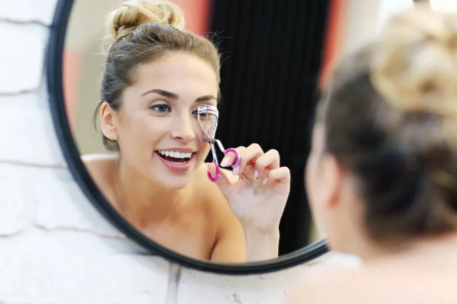 Picture of young woman using eyelash curler in bathroom