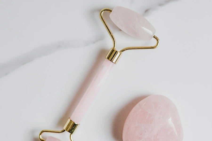 Pink and Gold Jade Roller on Marble Surface by Karolina Kaboompics