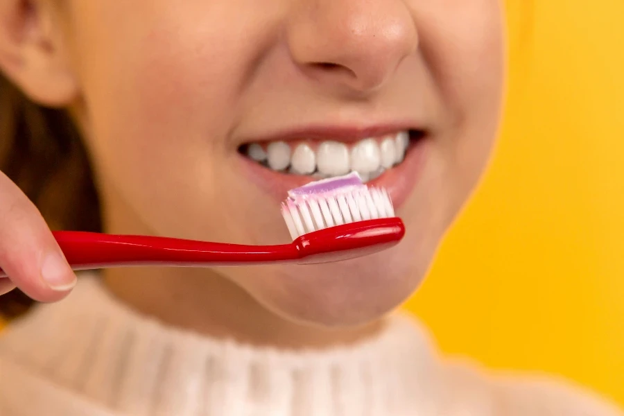 une belle fille se brosse les dents avec une brosse à dents rouge