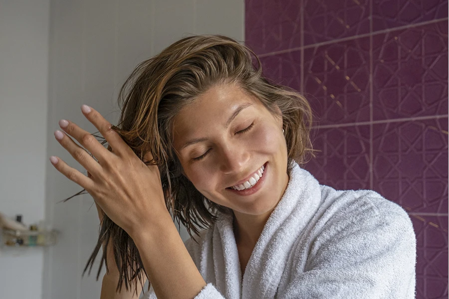 Ritratto di giovane bella donna in un bagno che esegue procedure cosmetiche dopo il bagno