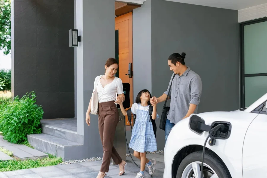 Progressive young parents and daughter with electric vehicle and home charging station