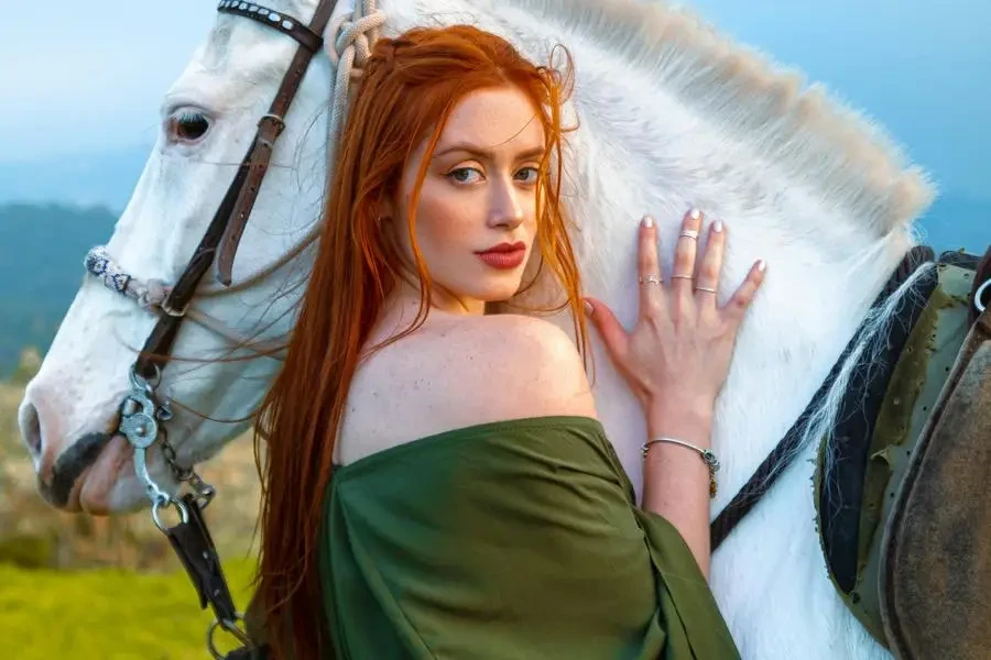 Mujer pelirroja vestida posando cerca del caballo blanco de Leandro Lopes