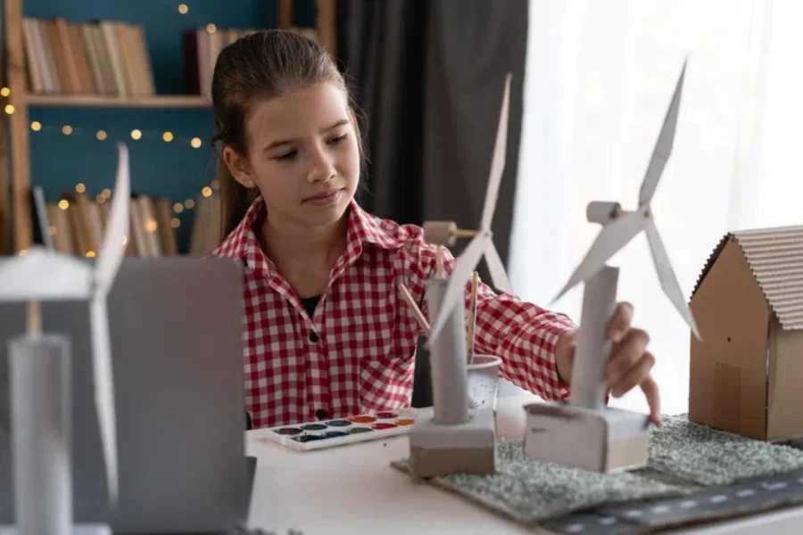 Artes escolares, niños inteligentes se divierten en un proyecto de artesanía, usando papel para construir una casa ecológica con turbinas eólicas