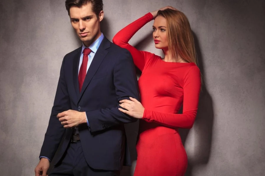 Genç ve zarif bir çiftin yan görünümü, kırmızı elbiseli kadın takım elbiseli ve kravatlı sevgilisine bakıyor.