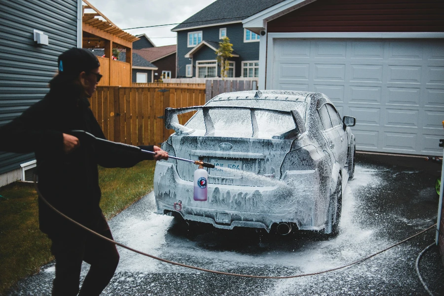 Side view of faceless male in black clothing washing car with foam