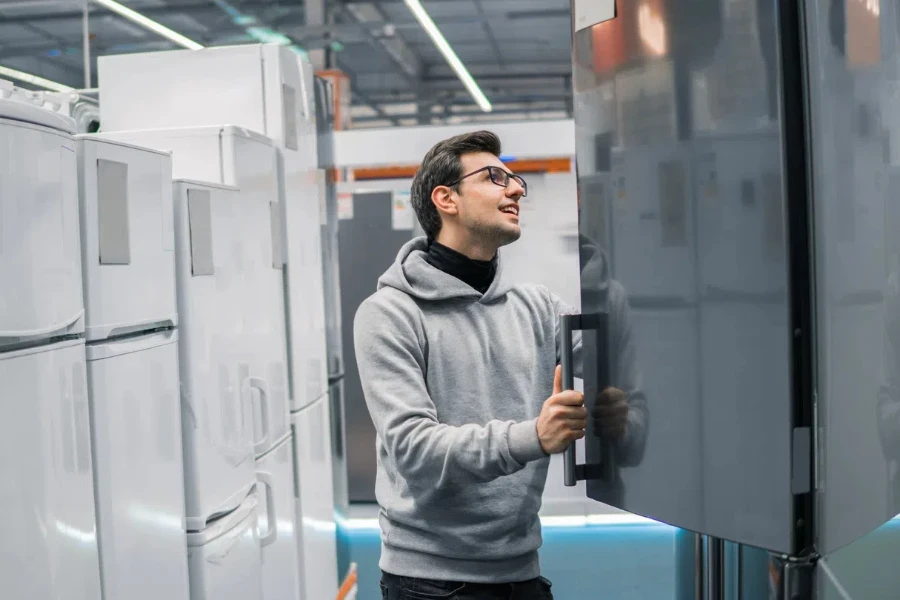 Smart modern male customer choosing large fridges in domestic appliances section