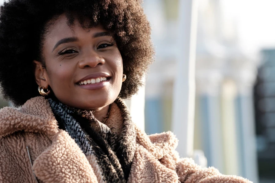 Jeune femme noire aux cheveux bouclés souriante regardant la caméra à l'extérieur