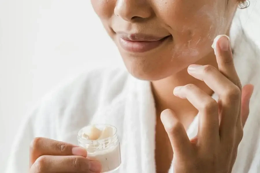 Smiling Woman Applying Facial Cream on Her Face by Greta Hoffman