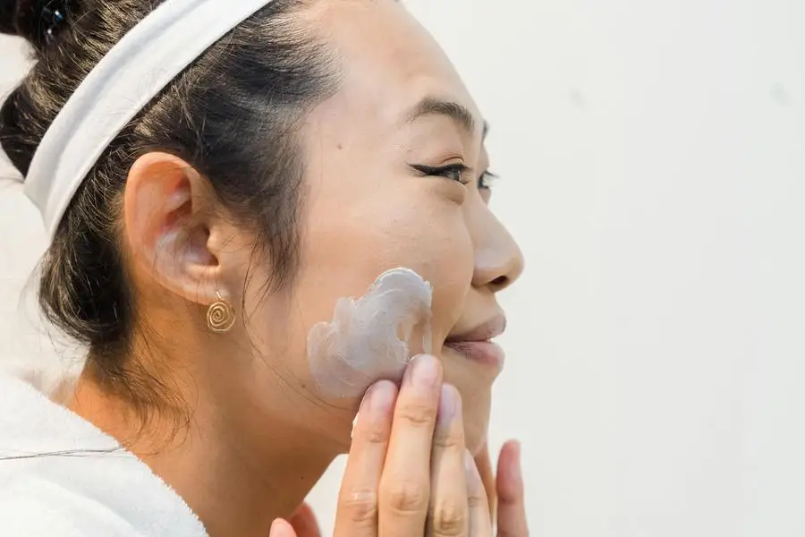 Donna sorridente che si applica la crema viso sul viso di Greta Hoffman