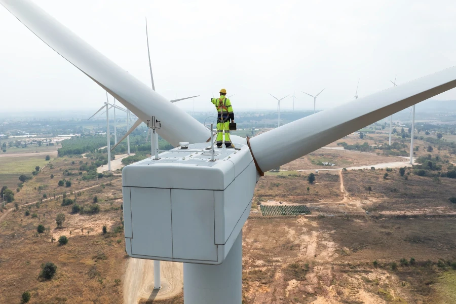 Ingeniero especialista en molinos de viento con chaqueta de seguridad verde y equipo de protección personal completo que incluye arnés de seguridad en la parte superior de la turbina eólica