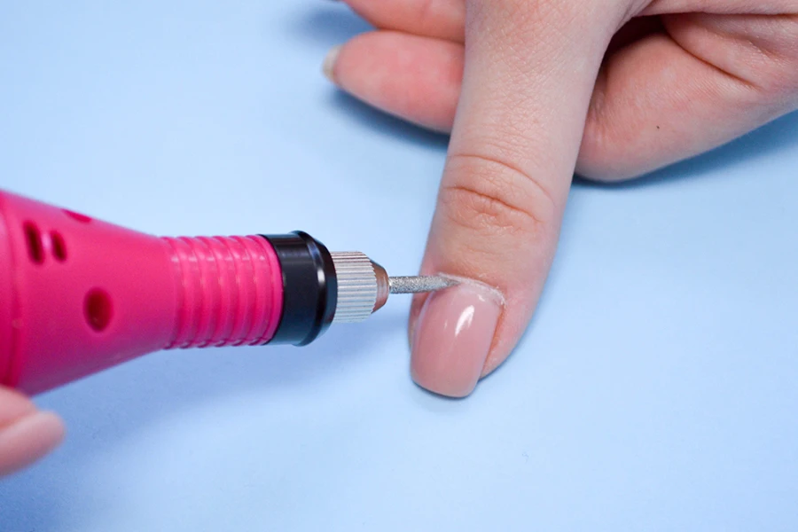 青い背景にネイルサロンで専用の機械で爪を加工する指の指に美しいマニキュアを施す過程