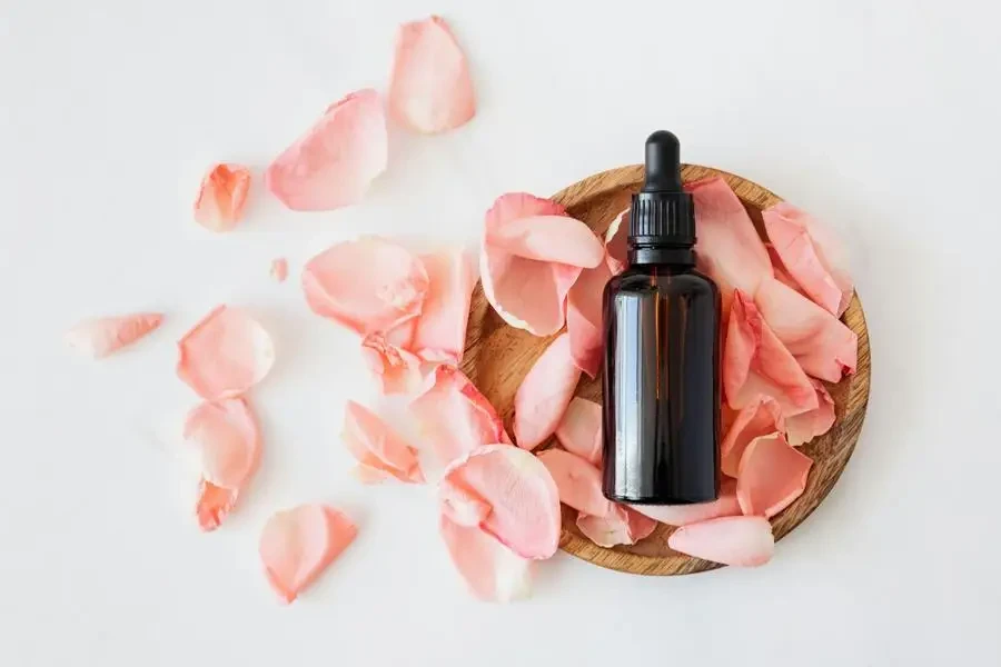 Vue de dessus d'une bouteille brune vide pour produit de soin de la peau placée sur une assiette en bois avec des pétales de rose roses fraîches sur fond blanc isolé par Karolina Kaboompics