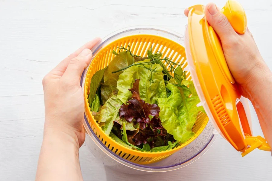 Top view of woman hands holding and drying salad in spinner tool bowl, healthy leafy greens inside.