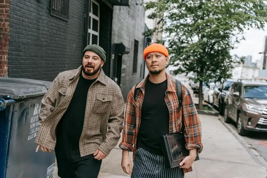 Two Men Wearing Plaid Shirts with Beanies Walking on Sidewalk by Anna Pou