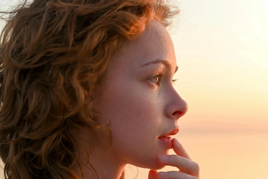 Donna rossa svestita con mano sul mento alla luce del tramonto