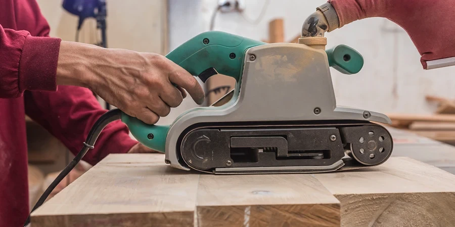 Het gebruik van een handschuurmachine of bandschuurmachine om het oppervlak van een gelijmd stuk hout voor een kast te egaliseren