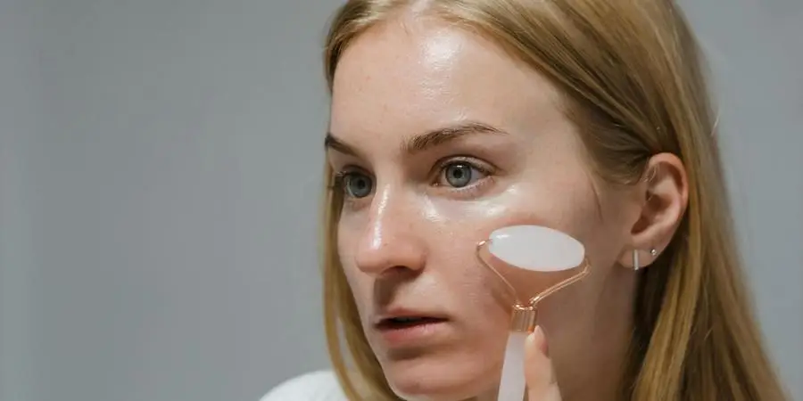 Mujer realizando un masaje facial con un rodillo de jade blanco por Polina Kovaleva