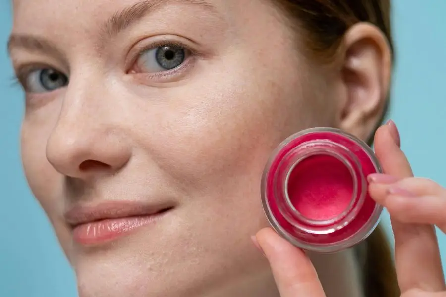 Woman Holding Red Round Glass Container Of Beauty Product by Ron Lach