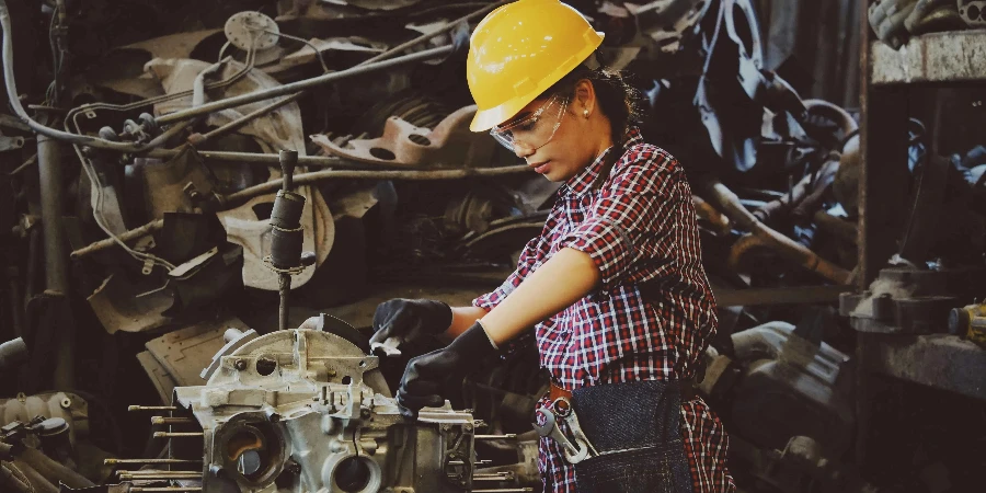 Woman Wears Yellow Hard Hat Holding Vehicle Part