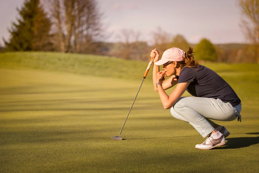 Mulher jogadora de golfe agachada e estudando o green antes de dar uma tacada