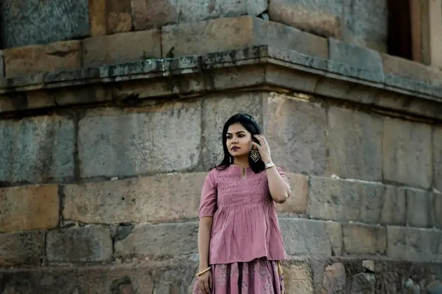 Conjunto de mujer vestida de rosa de pie bajo una esquina de piedra construida por Lalit Arora